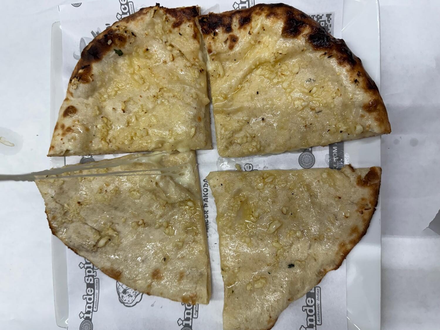 Melted cheese naan quartered on INDE SPICE branded paper
